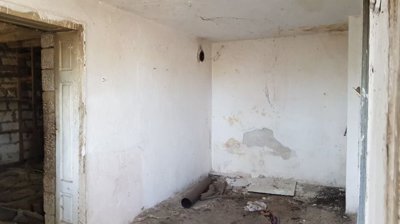 Interior view of a room with white walls, peeling plaster, and a window allowing natural light inside.