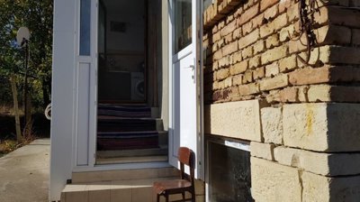 Entrance door with steps leading inside a small Bulgarian house showing brick and stone wall and a wooden chair outside