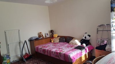 Bedroom showing a double bed with floral bedspread, pillows, and household items including a vacuum cleaner