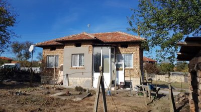 Side view of a small brick house with tiled roof and enclosed porch, dry garden and fencing