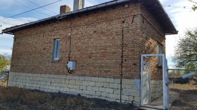 Side perspective of a small brick house showing stone foundation and metal gate entrance