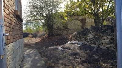 Pathway beside brick house with dry garden area, stone wall and trees