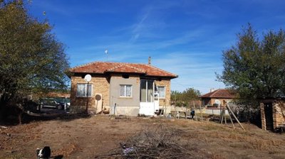 Front view of small brick house with tiled roof and fenced yard with dry garden