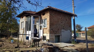 Side perspective of small brick house with enclosed porch and yard with trees