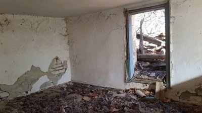Room interior showing damaged floor with exposed wooden beams and plaster walls with cracks