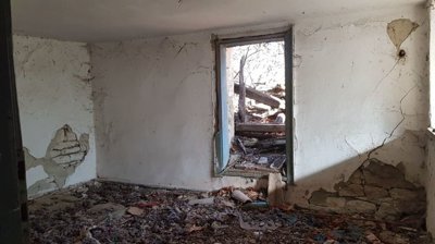 Interior of a room with cracked plaster walls, debris scattered on the floor, and an open doorway leading outside.