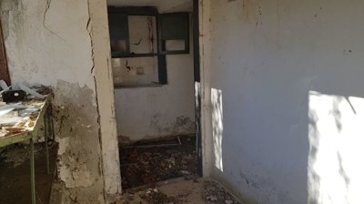 Room interior showing white plastered walls with some damage and debris scattered on the floor