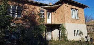 Two-storey rural house built from brick and stone with ivy climbing on the walls and white framed doors and windows under a blue sky.