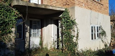 Close-up view of the entrance area of a two-storey rural house showing white doors, windows, and ivy growing on the walls.