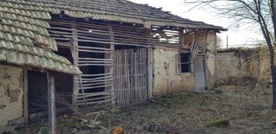 An old wooden outbuilding with slatted walls and a tiled roof located in the yard of the rural property.