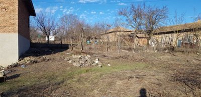 Open rural yard showing dry grass, scattered branches, and several old brick and wooden outbuildings in the background.