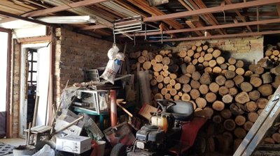 A storage room featuring a large stack of firewood and a red lawn tractor under a wooden ceiling.