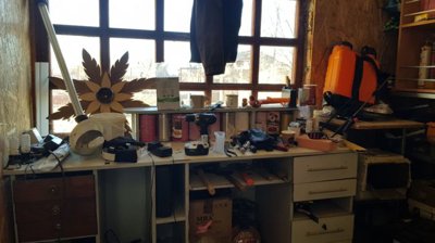 A workshop space featuring a workbench cluttered with tools and storage cabinets mounted on the wall.