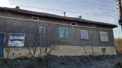Front side of a Bulgarian village house showing stone foundation and plastered walls with multiple windows