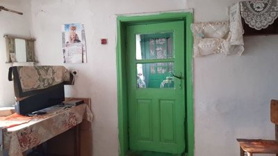 Room featuring a green door, calendar with a cat image, and a table with a TV covered by a cloth.