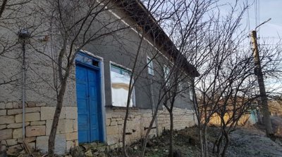 Front view of the house showing stone base, plaster walls, blue door, and leafless trees