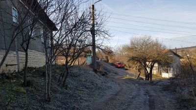Dirt road running alongside a house with stone base and leafless trees lining the roadside