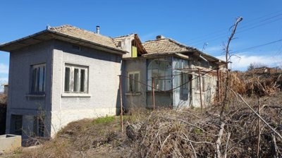 View of the house exterior showing tiled roof, plastered walls, and surrounding dry vegetation