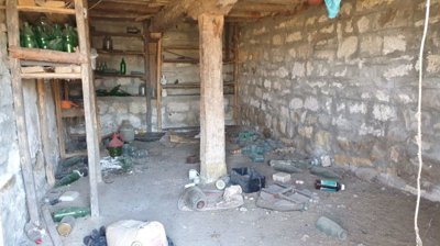 Basement area with stone walls, wooden shelving, and various glass bottles on the floor and shelves