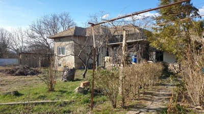 Rural house with plastered walls surrounded by garden area and leafless trees under clear sky