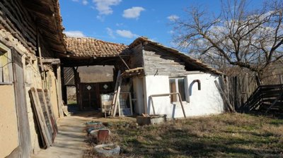 View of the rustic Bulgarian house showing wooden and stone construction with tiled roof and outdoor yard area