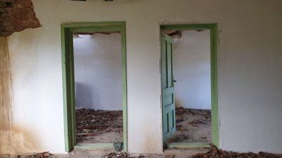 Interior showing two green doorways leading to empty rooms with debris on the floor
