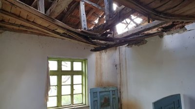 Interior view of a room with a damaged ceiling exposing wooden beams and broken roof tiles.
