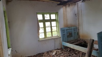 Interior of a room featuring an old blue wooden bed frame and a damaged ceiling with exposed wooden beams.