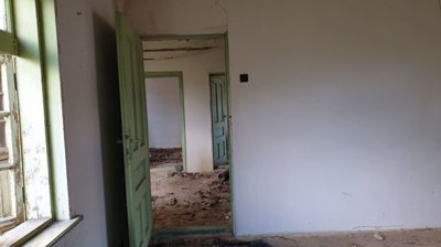 Interior view showing green door frames leading to multiple empty rooms with debris on the floor