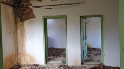 Empty interior room with green door and window frames, white walls, and wooden ceiling