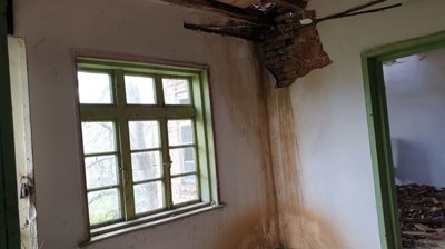 Room interior showing damaged ceiling, green window and door frames, and white walls