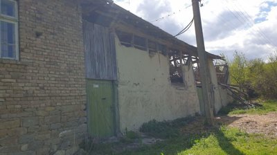 Side view of an old house showing plaster and brick walls, a green door, and a collapsed roof section.