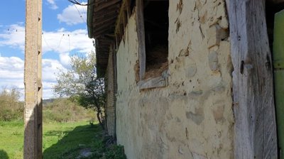 Narrow passageway between two stone walls featuring a wooden door and a window opening filled with hay.