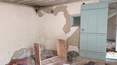 Room interior showing peeling plaster walls, a light blue wooden door and window, and debris scattered on the floor