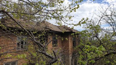 Exterior view of an old brick house with a tiled roof surrounded by leafing trees