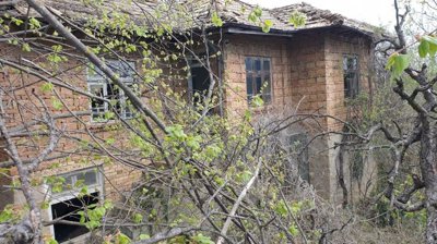 Exterior view of an old brick house with a tiled roof surrounded by leafing trees