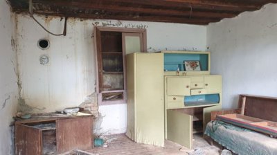 Room featuring old wooden furniture including a cupboard and a bench with peeling walls and exposed ceiling beams.