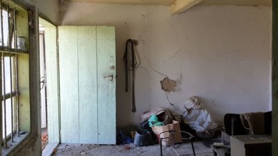 Interior storage room with a green wooden door and window, containing boxes, bags, and miscellaneous items.