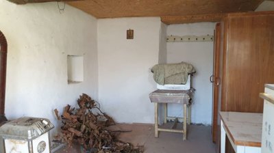 Interior room containing a wood stove, cupboard, wardrobe, and covered items on the floor and furniture.