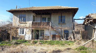 Front facade of an old Bulgarian house showing wooden balcony, windows, and garden space