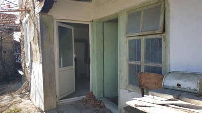Entrance to the house with open door, window, and outdoor table with chair nearby