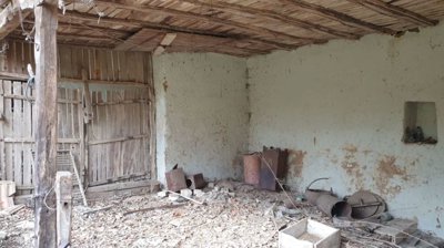 Interior view of a rustic barn featuring wooden beams, a dirt floor, and scattered old items and debris.