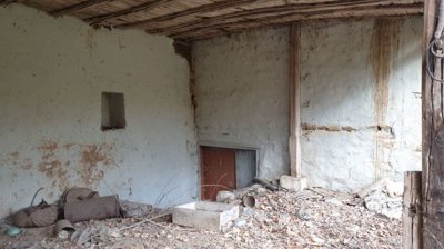 Barn interior showing plastered walls, wooden support beams, and dirt floor with scattered debris.