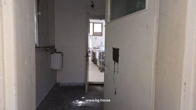 Narrow interior corridor with an open door leading to a brighter room with windows