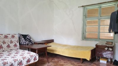 Interior view of a room furnished with a single bed, sofa, small tables, and a window with wooden shutters
