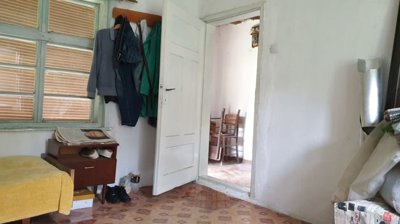 Room interior with open door leading to another room, showing furniture and coats hung on hooks