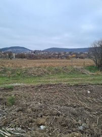 View of ploughed agricultural land with hills and village houses in the background under a cloudy sky.