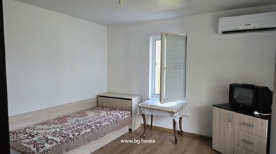 A bedroom featuring a single bed with patterned bedding, a small table by an open window, a TV on a cabinet, and an air conditioning unit on the wall.