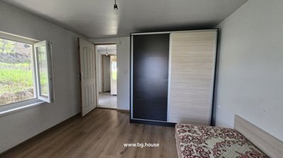 A bedroom containing a large sliding door wardrobe, a single bed with patterned bedding, an open window, and a door leading to a hallway.