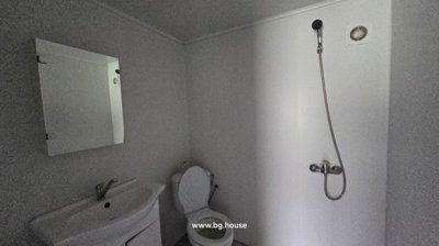 A bathroom featuring a toilet, a white sink with cabinet, a wall mirror, a showerhead, and a ventilation vent.